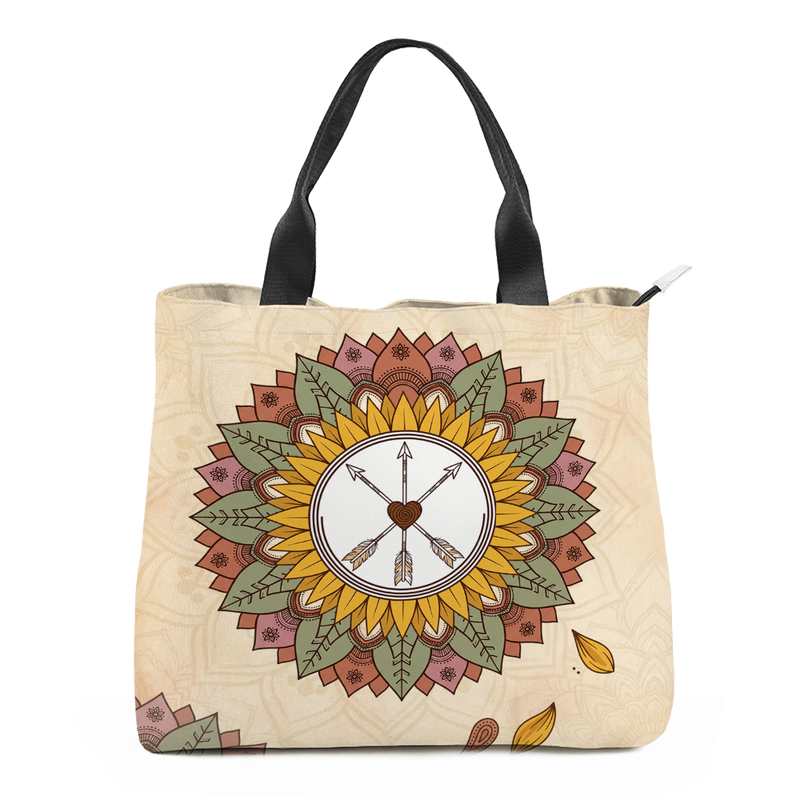 Joni Tote Bag mockup - sunflower mandala centred on cream, a white disc at its heart holding three crossed arrows and a brown spiral heart, golden petals ringed by olive-green leaves and terracotta and dusty-rose outer petals, black webbing handles