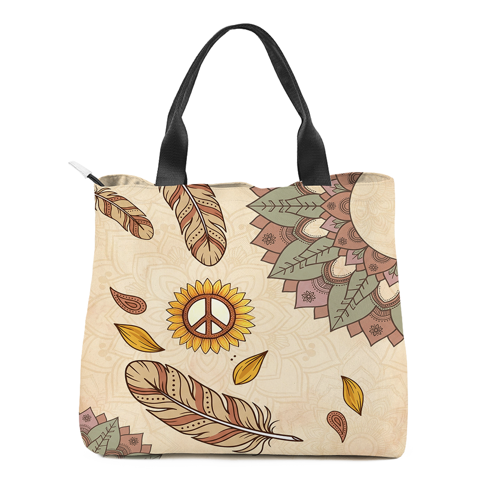 Joni Tote Bag mockup - the second face, the mandala pushed into opposite corners and cut by the edge, three tan and rust dotted feathers falling loose, a sunflower with a dotted peace sign at its centre, rust paisley teardrops and mustard leaves scattered across cream, black webbing handles