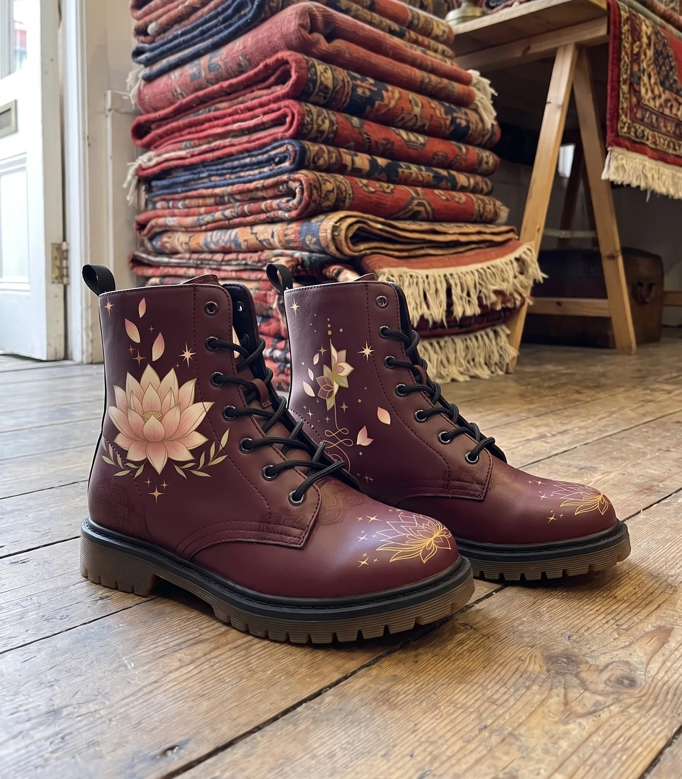 Burgundy lotus boots on a wooden floor in front of a stack of folded patterned rugs