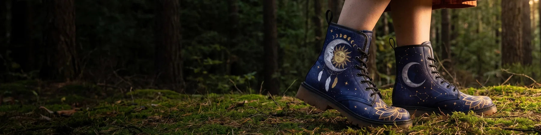 Navy sun and moon boots worn on moss at the edge of a dark forest, with open woodland to the left