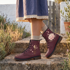 Lotus Leather Boots — laced on and standing among lavender on a stone step, cream socks and a navy lace-hem skirt above them, an olive branch to the side, open lotus and gold unalome on wine