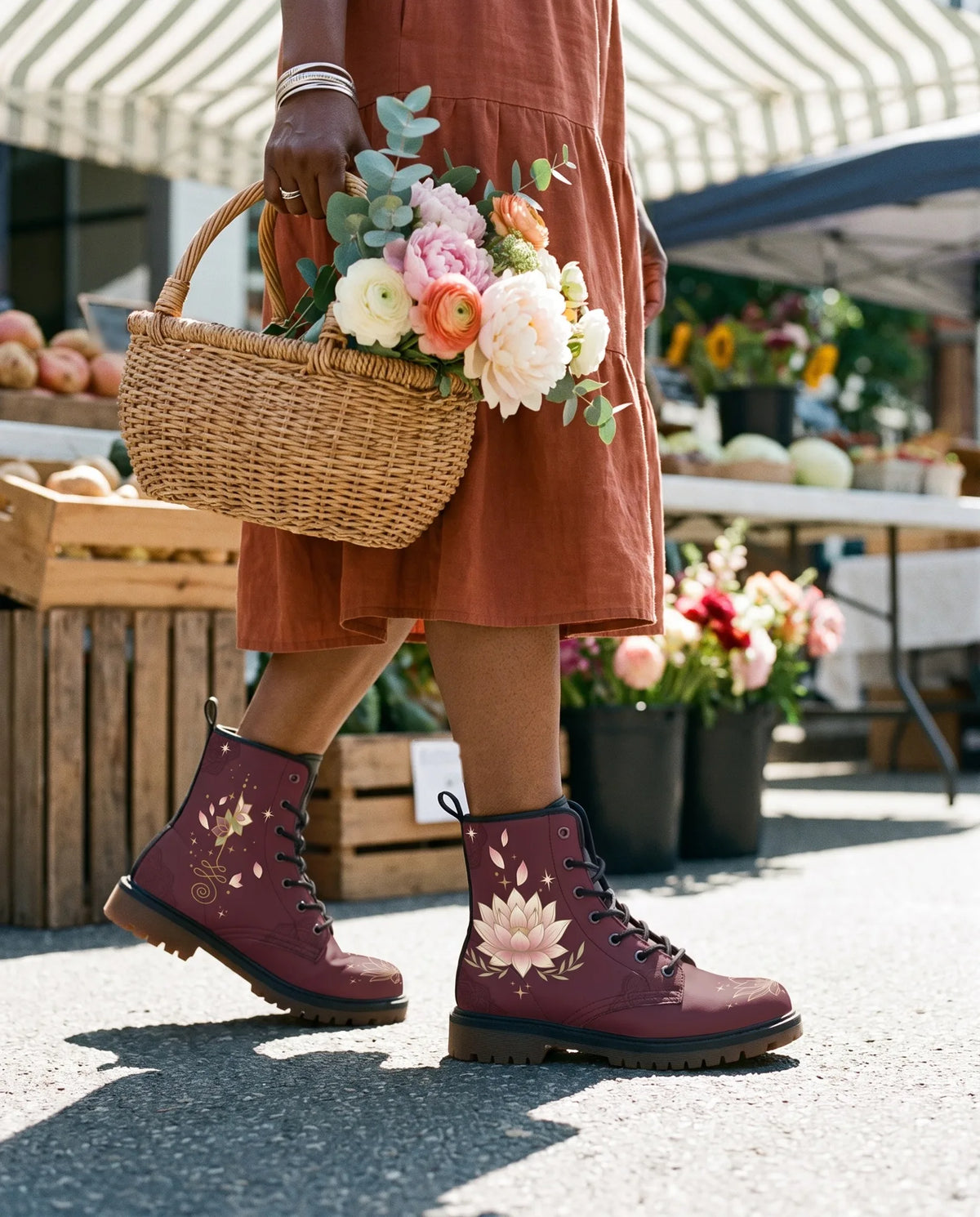 A woman in a rust linen dress walks through a sunny farmers market with a basket of peonies, wearing burgundy Lotus boots